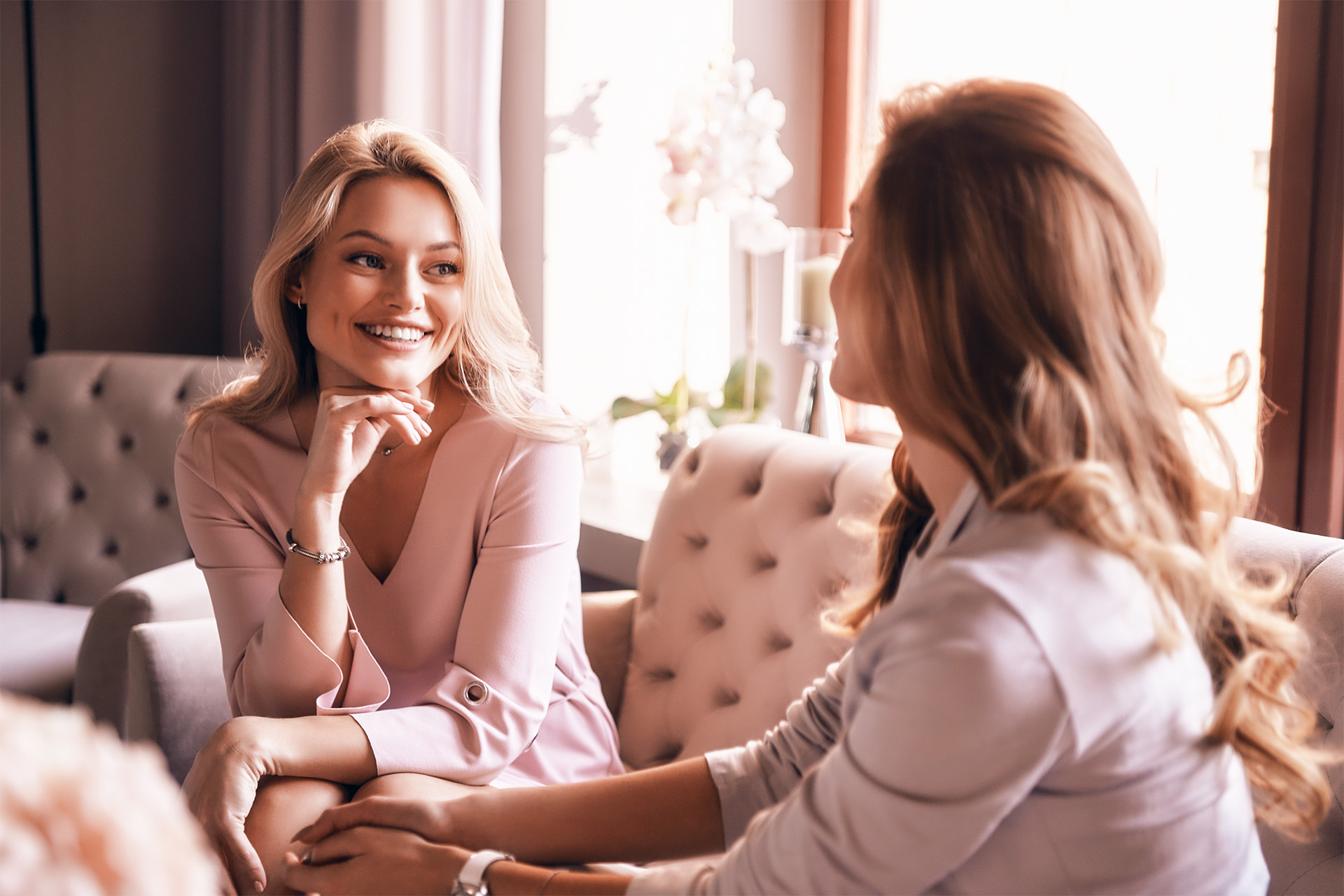 beautiful joung woman with blonde hair and blue eyes sitting on the sofa and talking to another joung woman with long brown hair