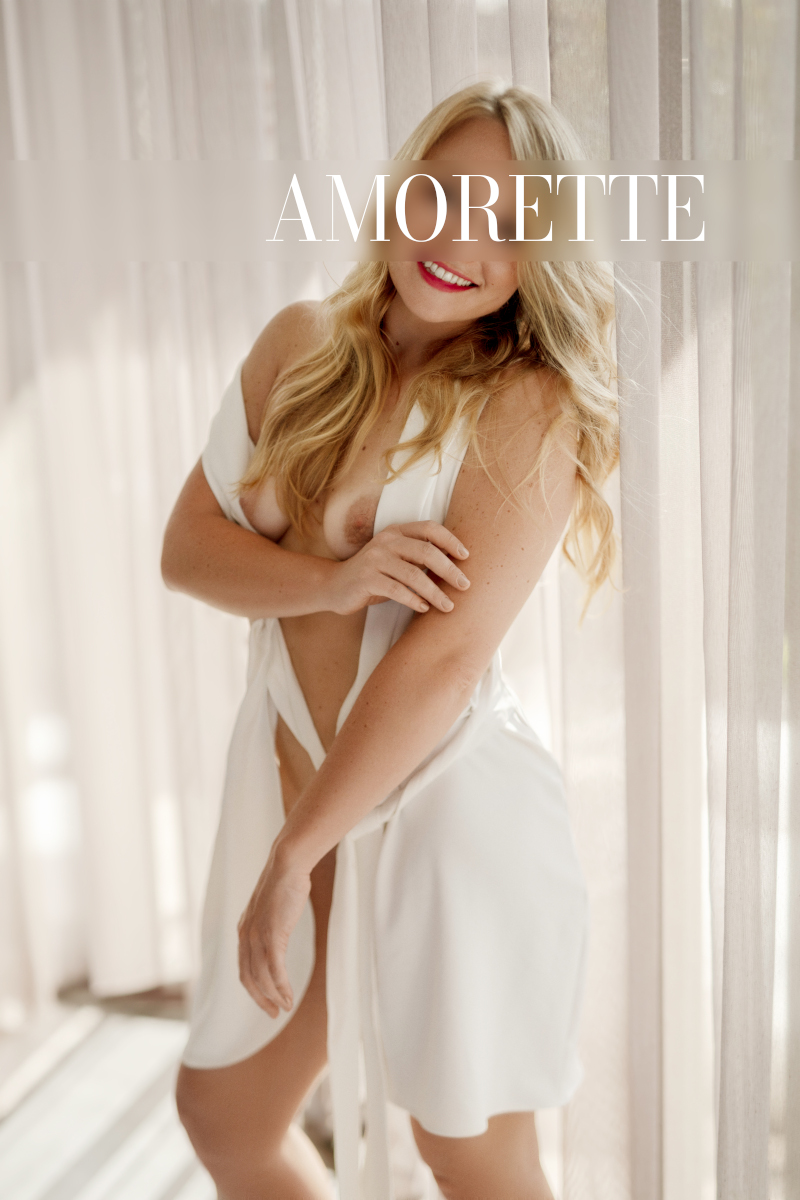 Elite escort model Ella from Berlin displays her natural breasts in an elegant white dress.