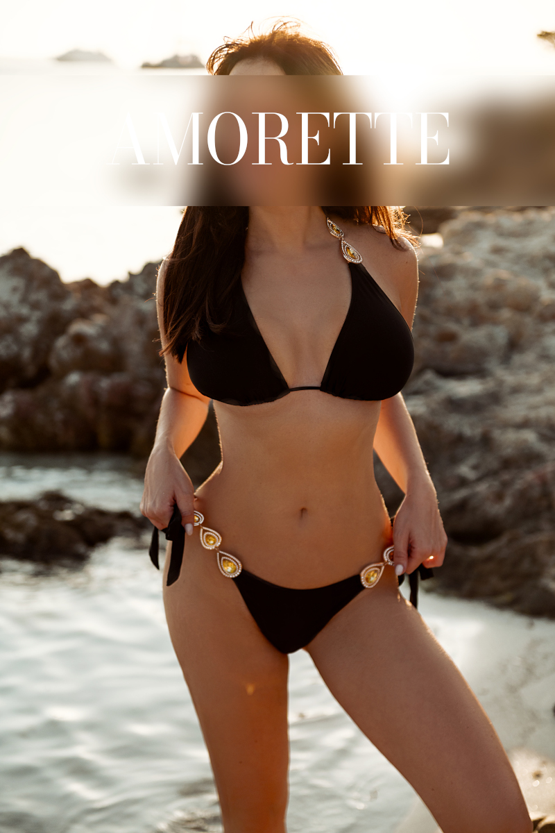 elite escort model eden munich in a black bikini on the beach, her long darkbrown hair is open and straight