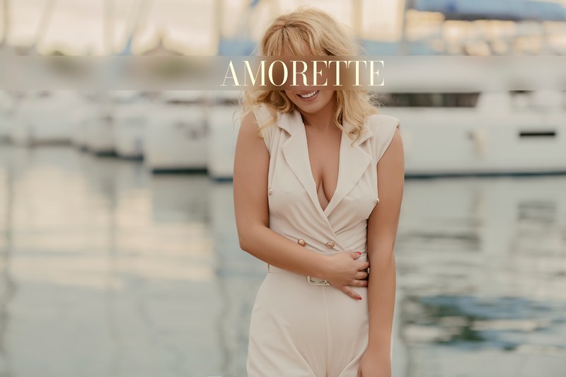 mariella international high class escort 44 elite escort model mariella from cyprus shows her from the front while standing in front of a boat at the harbour wearing a white overall and showing her natural breasts without bra, her blonde hair is open and weavy, she shows her beautiful smile, red nails, natural high class escort, international, blonde escorts, luxury, summer