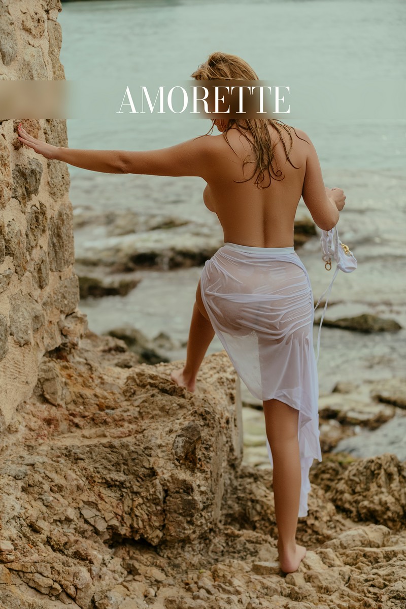 mariella international high class escort 54 elite escort model mariella from cyprus shows her from the back while standing on the rocks at the beach, her blonde hair is wet and wavy, natural high class escort, international, blonde escorts, luxury, vacation, red nails