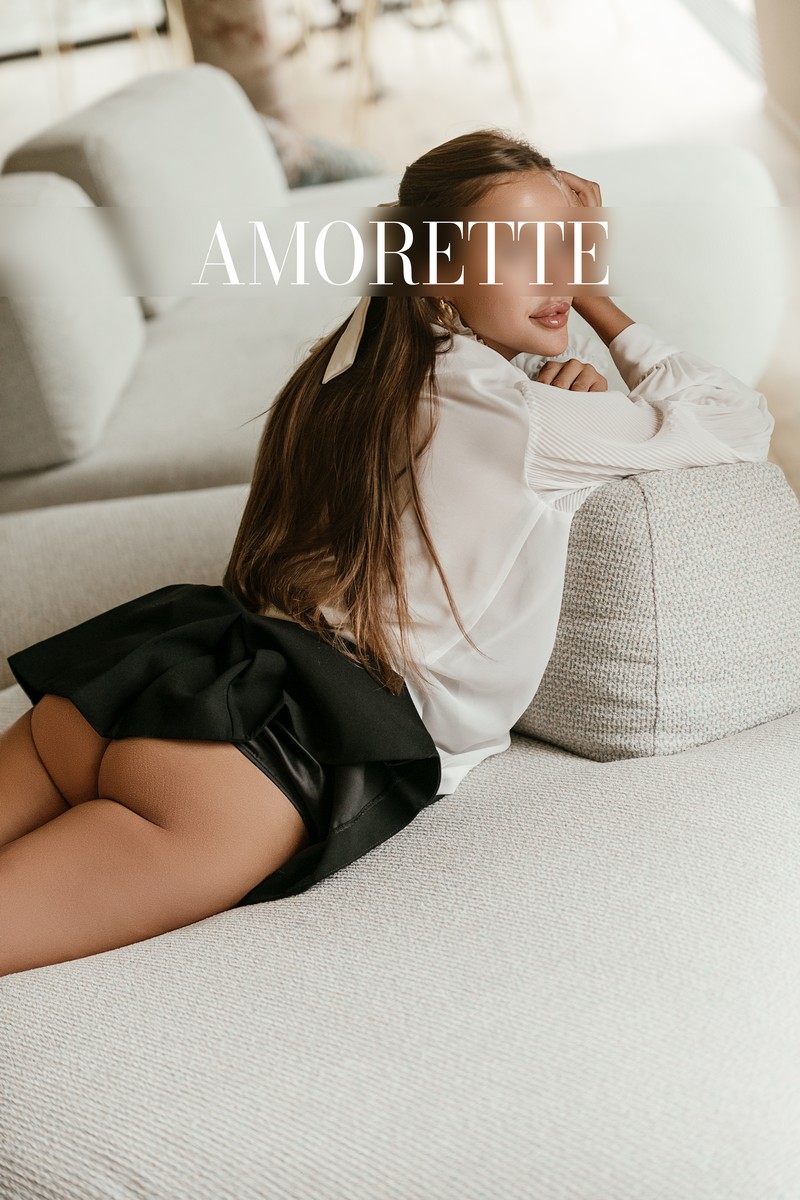 Alina – Elite Escort Model from Frankfurt alina elite escort model from frankfurt shows her from the back while laying down on a white sofa wearing a elegant outfit, black skirt and white shirt, she shows her round butt, natural, her long bworn hair is open and smooth, high class escort, international, elite models, elite model, luxury, vacation, traveling