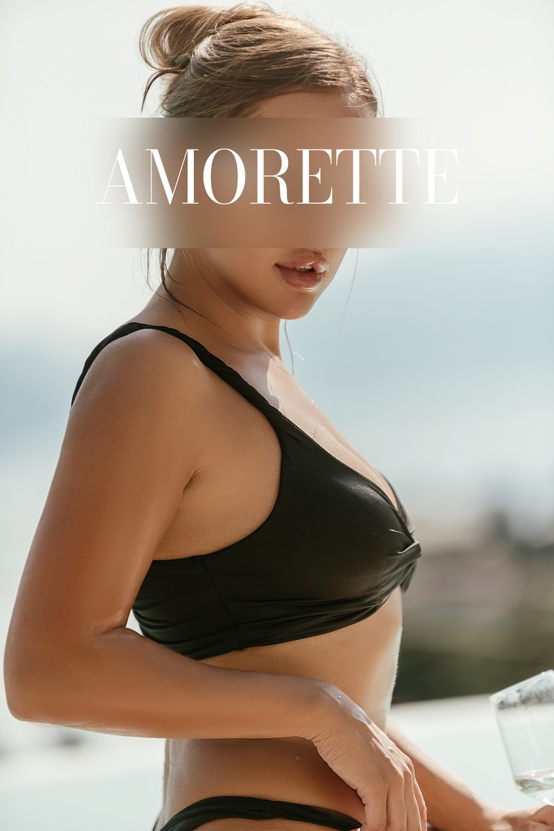 Alina, an elite escort model from Frankfurt, shown in side profile wearing a black bikini, showcasing her perfectly toned skin and athletic body. Her long brown hair is tied up. Natural escort, high-class escort, international, luxury, vacation, summer.