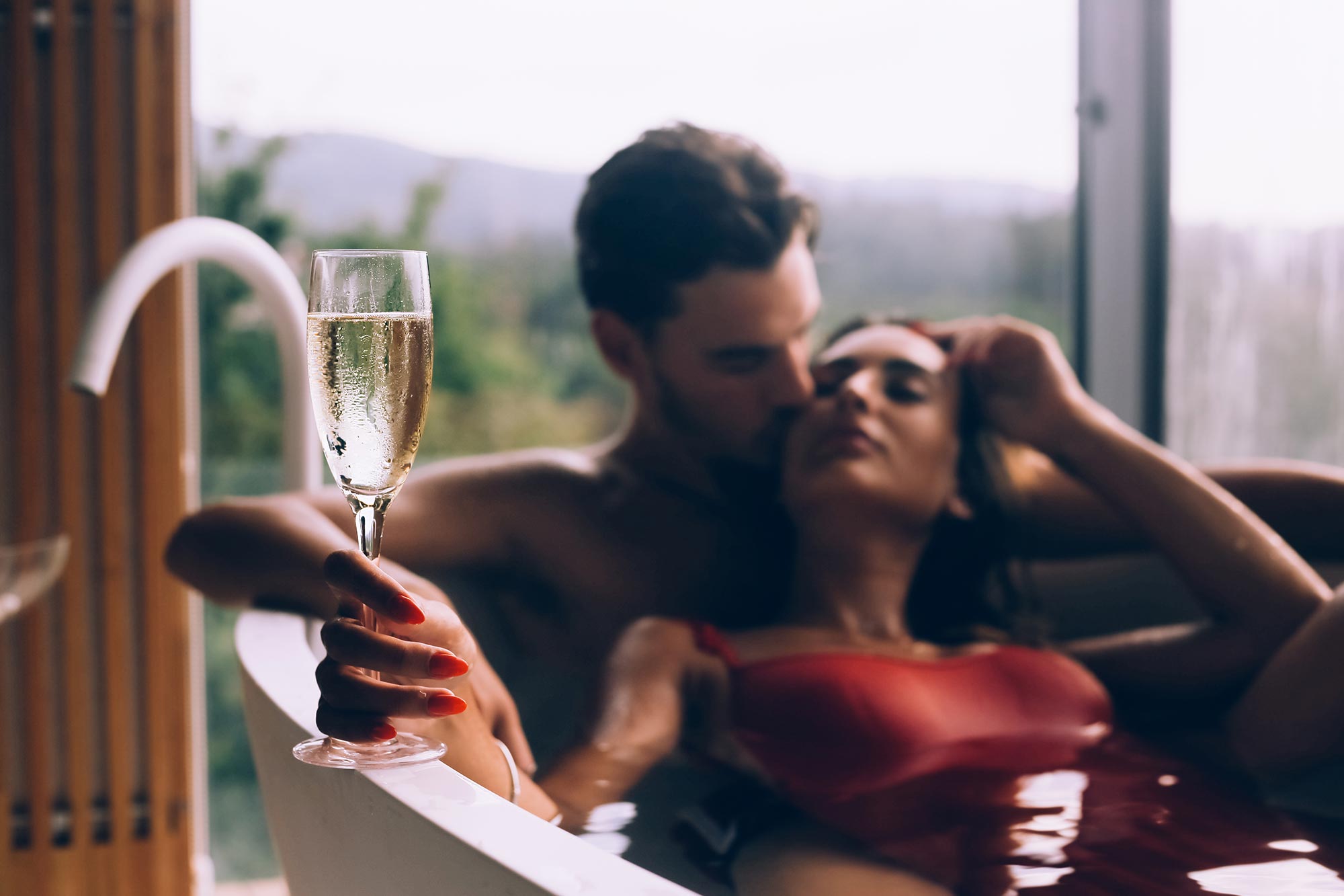 amorette international elite escort agency, high class escort service, couple lying in a bathtub, romantic, glass of champagne, red swimsuit, red nails, loving couple, young couple, dating, date, escort date, luxury, traveling, vacation