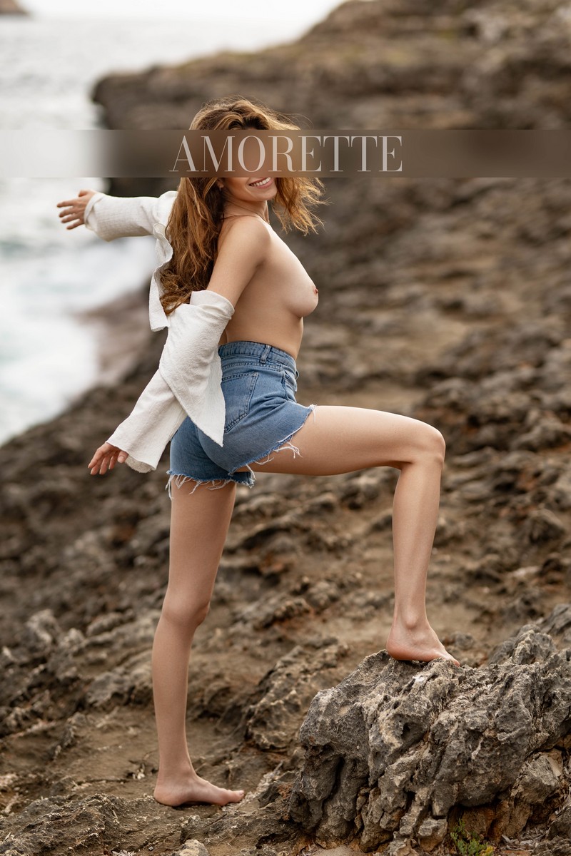 Ellie – Elite Escort Model from Florida Elite escort model Ellie from Florida stands confidently on sunlit rocks with the sparkling ocean as a dramatic backdrop. She wears stylish jean shorts that highlight her toned silhouette, one leg gently resting on a rock, while both hands are lifted behind her head in a playful, poised gesture. Her bright, radiant smile exudes warmth, confidence, and premium allure. Soft natural light illuminates her figure, emphasizing the polished lines of her silhouette and the relaxed elegance of her outfit. The rugged coastal setting and vibrant ocean enhance her adventurous spirit, elegance, and international sophistication. High-class escort model, luxury, traveling, USA, America, international, elegant lingerie, lingerie, models.