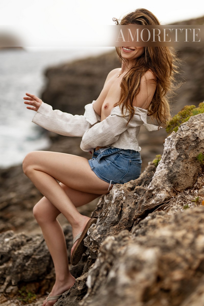 Ellie – Elite Escort Model from Florida Elite escort model Ellie from Florida sits gracefully on a sunlit rock, the vast ocean stretching behind her. She wears a casual yet chic white long-sleeve shirt tied around her waist and simple flip-flops, complementing her natural, relaxed silhouette. Her long hair cascades freely in the breeze, and her wide, radiant smile exudes warmth, confidence, and premium allure. The soft natural light highlights the polished lines of her figure and the casual textures of her outfit, while the dramatic coastal scenery emphasizes her adventurous spirit, elegance, and international sophistication. High-class escort model, luxury, traveling, USA, America, international, elegant lingerie, lingerie, models.